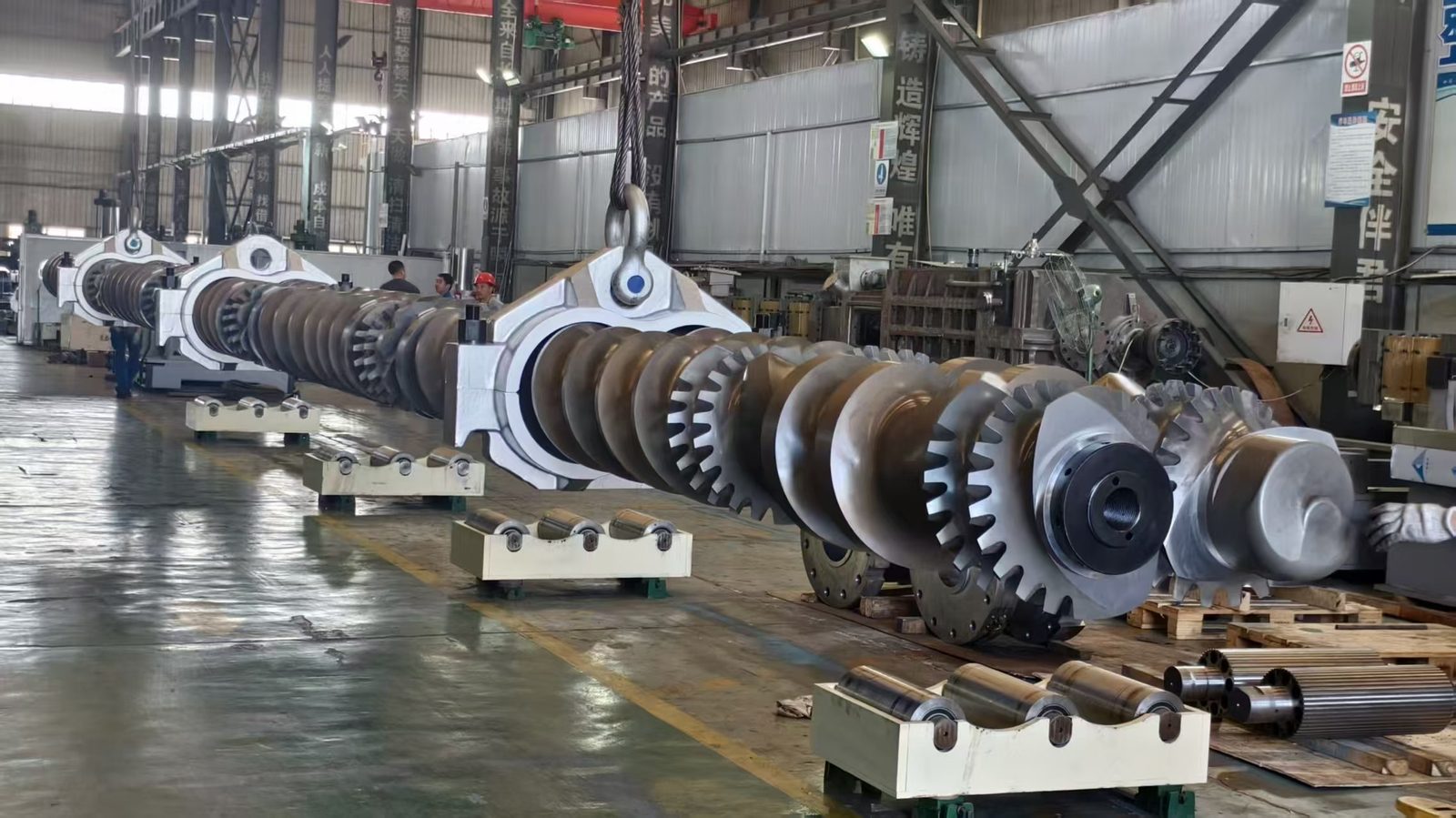 Large screw assembly being handled by overhead crane in factory